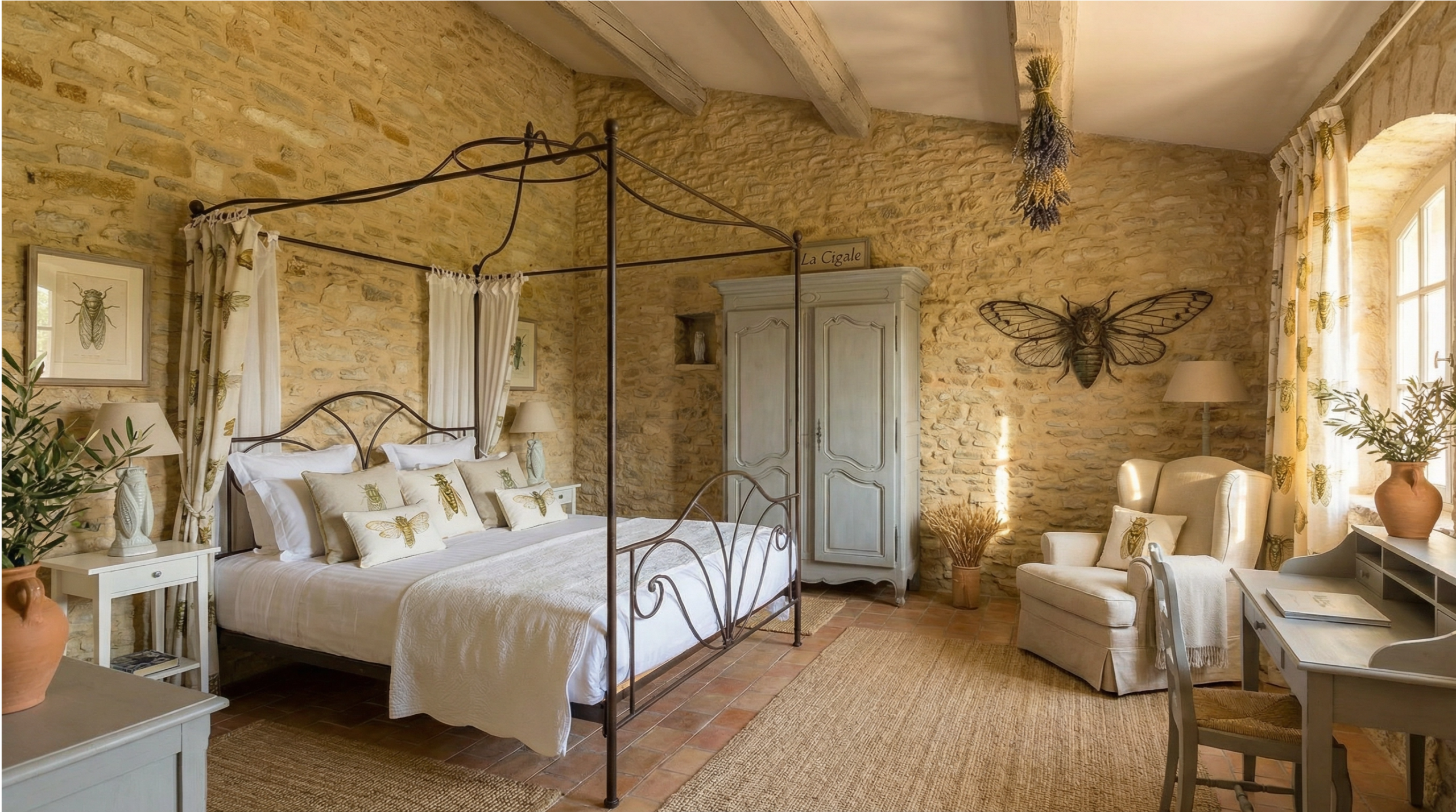 Chambre « Lavande » rustique et apaisante : lit double en fer forgé blanc, murs en pierre apparente, poutres en bois, sol en terre cuite et décoration sur le thème de la lavande, avec un bouquet dans un vase et un tableau de champ de lavande.